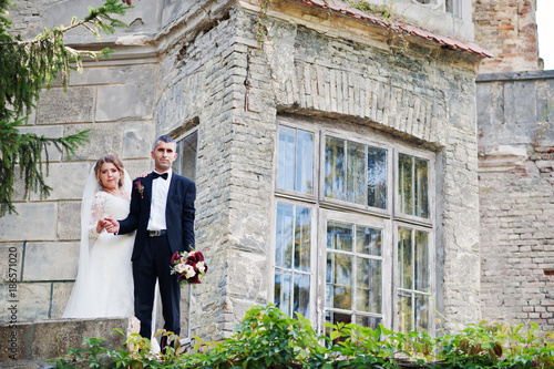 Romantic lovely newly married couple posing by the medieval castle on their wedding day.