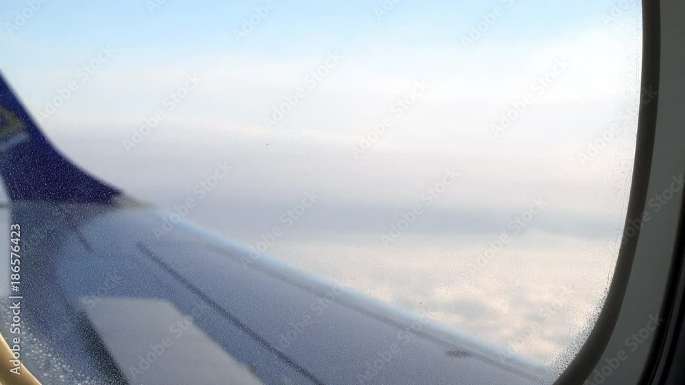Blur view from airplane window with wing and cloudy sky behind. Selective focus on the window Blur view from airplane window with wing and cloudy sky behind. Selective focus on the window