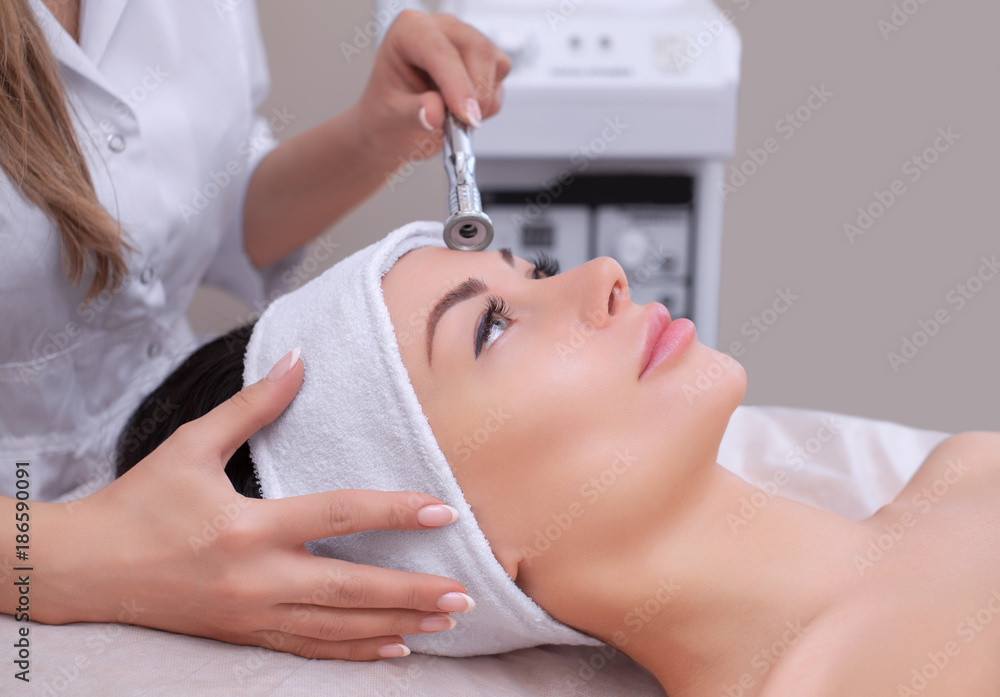 The cosmetologist makes the procedure Microdermabrasion of the facial skin of a beautiful, young woman in a beauty salon.Cosmetology and professional skin care. The cosmetologist makes the procedure Microdermabrasion of the facial skin of a beautiful, young woman in a beauty salon.Cosmetology and professional skin care.