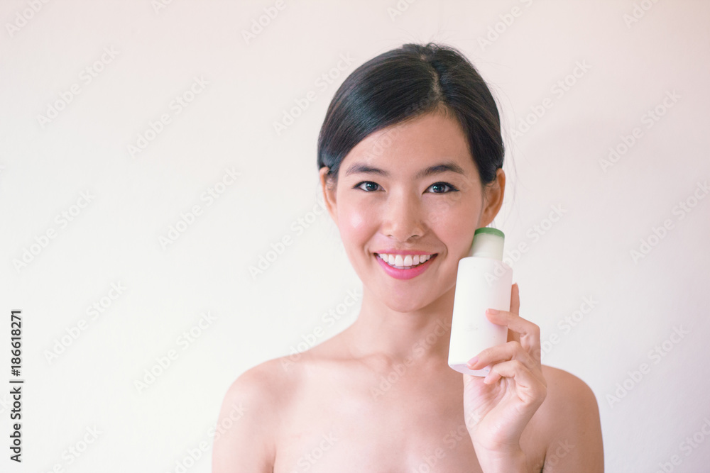 Beauty Skincare concept- Young Asian woman after shower smiling holding a bottle of skincare product Beauty Skincare concept- Young Asian woman after shower smiling holding a bottle of skincare product