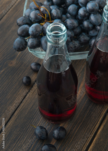Glass bottles of fresh young red wine with a bunch of black grapes