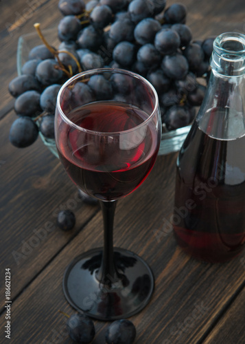 A wineglass of fresh young red wine with glass bottles and a bunch of black grapes