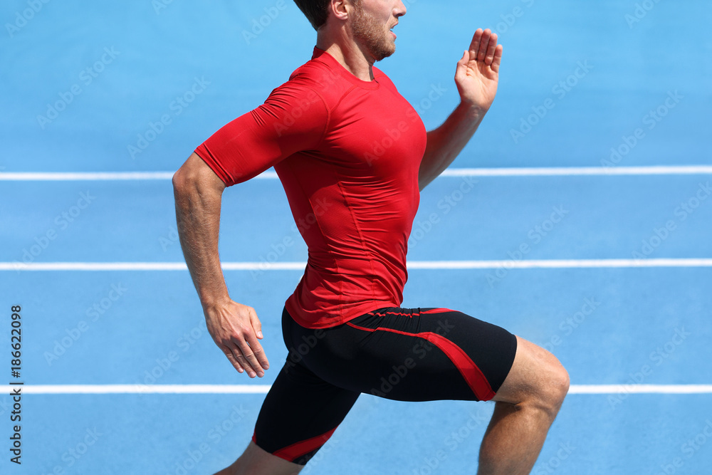 Athlete runner running on athletic track training cardio. Jogger man  jogging fast pace for competition race on blue outdoor stadium tracks  wearing red compression sport clothes. Male person fit body. Stock Photo
