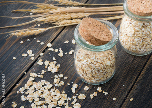 Raw oat flakes or oat ears cereals in craft glass jars with oat spikes or spikelets photo