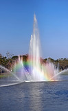 rainbow on fountain water surface in park with blue sky background