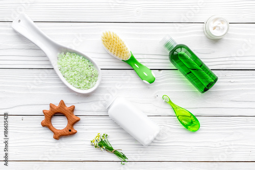 Children's means hygiene with chamomile. Bottles, spa salt, tooth brush and toy on white wooden background top view