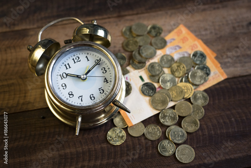 time is money concept - golden bell clock,money and coins on a wooden table background 