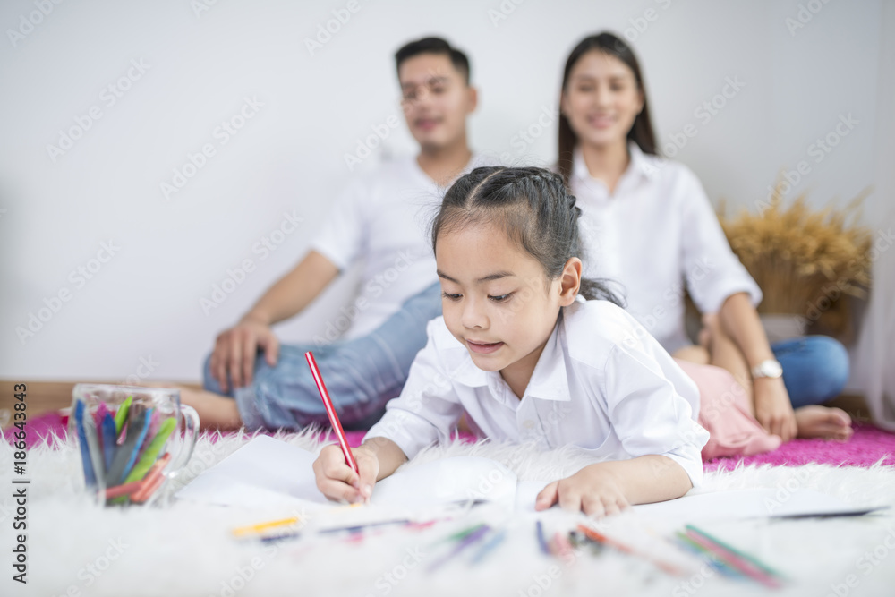 Fototapeta premium Asian father and mother looking daughter child painting color on book
