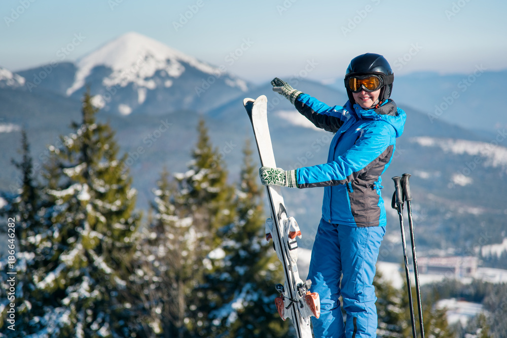 Shot of a smiling woman skier standing on top of a mountain at ski resort, pointing at stunning natural winter landscape surrounding her copyspace enjoyment happiness recreation seasonal sport