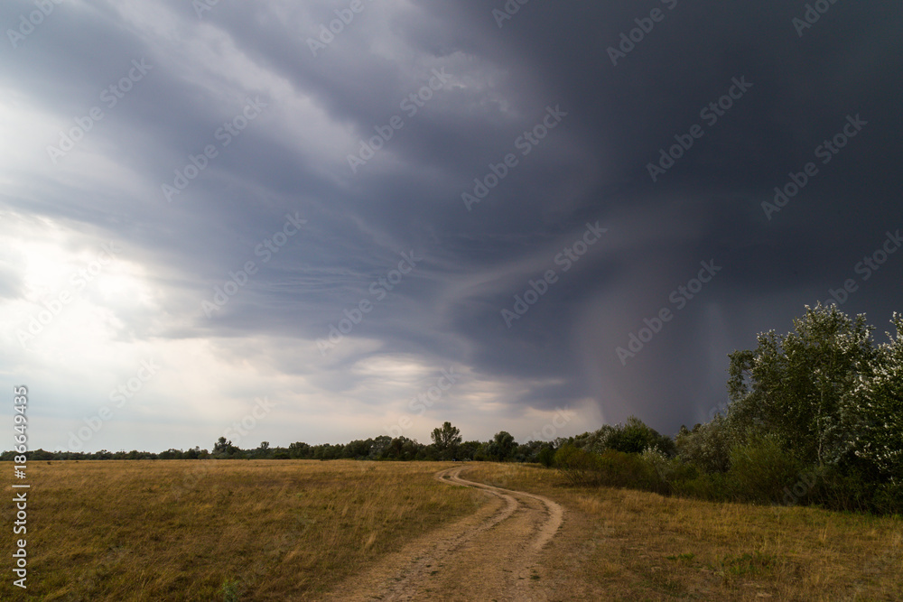 Dramatic storm and microburst cloud with rain over country road in rural area