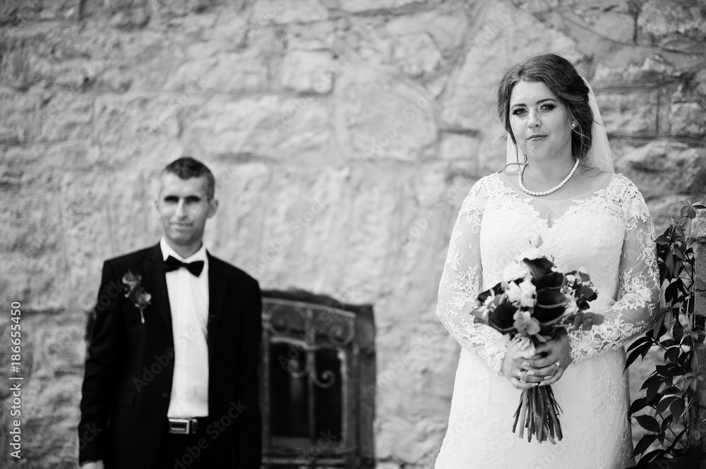 Romantic lovely newly married couple posing by the medieval castle on their wedding day. Black and white photo.