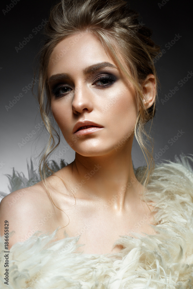 Young blonde girl with hairdo and creative makeup. Beautiful model in a fur coat. Shining skin. Evening image. Beauty of the face. Photo is taken in the studio. Young blonde girl with hairdo and creative makeup. Beautiful model in a fur coat. Shining skin. Evening image. Beauty of the face. Photo is taken in the studio.