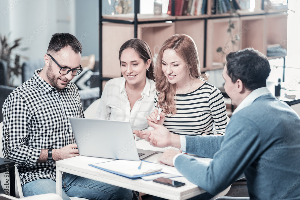 Let me explain. Nice-looking stylish smiling employees sitting in the office by the table using the laptop and listening to the colleague. Let me explain. Nice-looking stylish smiling employees sitting in the office by the table using the laptop and listening to the colleague.
