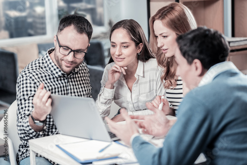 Collective creativity. Four smart occupied concentrated workers sitting together in the room using the laptop and looking at the screen.