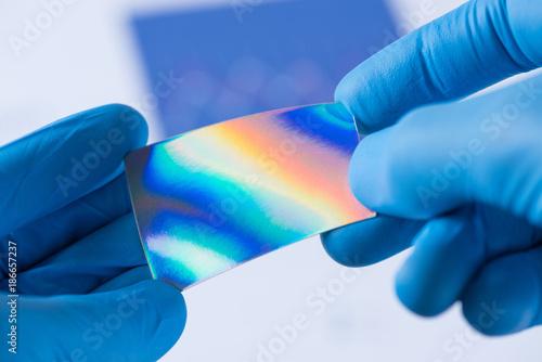 Piece of new type of material or thin coating on plastic with improved properties in laboratory in scientist hands, iridescent and pressure sensitive photo