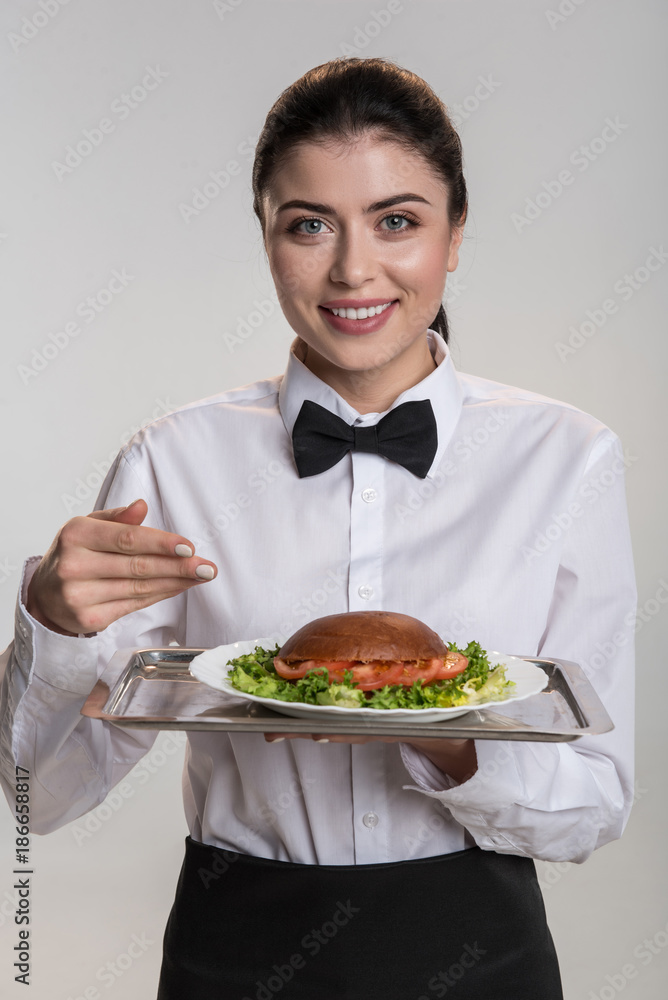 Delicious dish. Beautiful gay glad woman introducing dish while posing and staring at the camera Delicious dish. Beautiful gay glad woman introducing dish while posing and staring at the camera