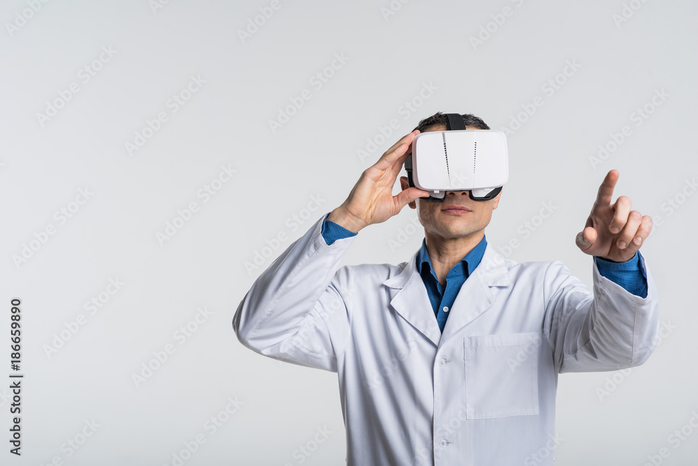 Modern technology. Pensive creative male doctor trying VR glasses while gesturing and wearing lab coat Modern technology. Pensive creative male doctor trying VR glasses while gesturing and wearing lab coat