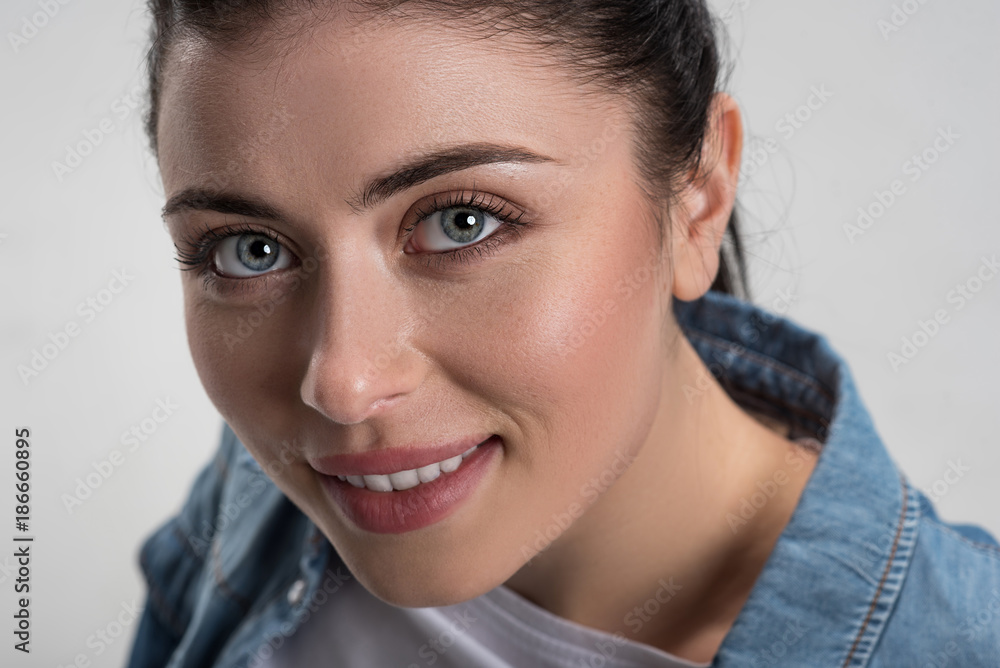 Charming smile. Close up of ambitious happy female face when woman smiling posing on the grey background while gazing at the camera Charming smile. Close up of ambitious happy female face when woman smiling posing on the grey background while gazing at the camera