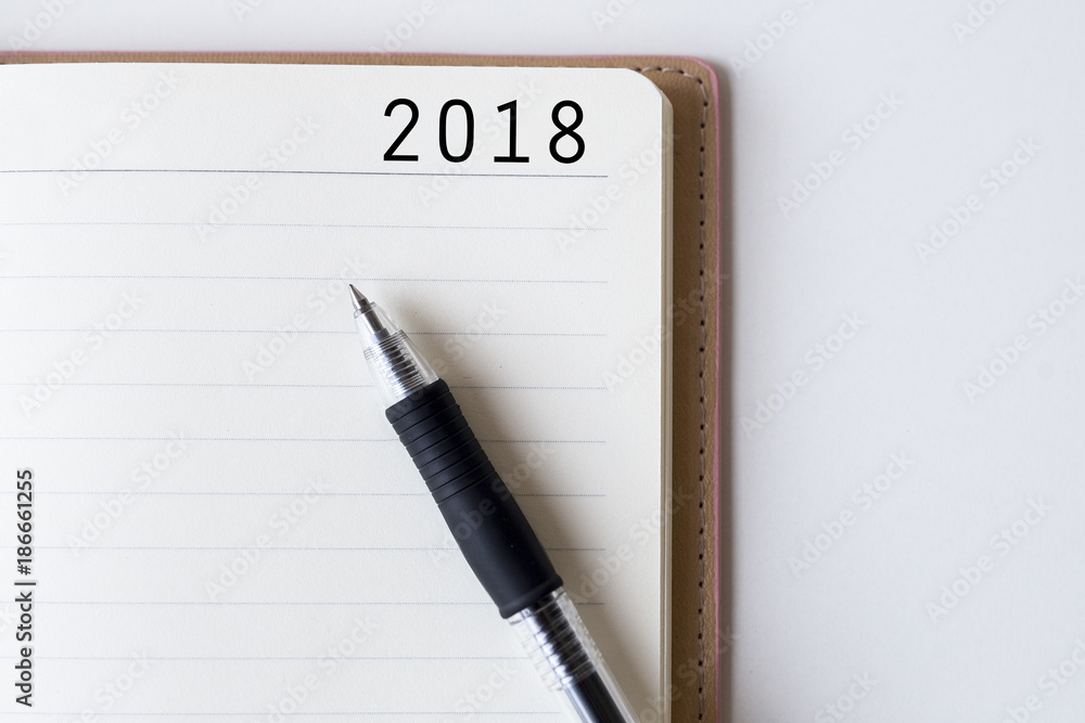 Conceptual,notebook on a white table. open diary and pen with 2018 words Conceptual,notebook on a white table. open diary and pen with 2018 words