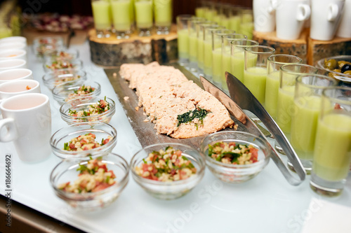 A buffet table with a variety of appetizers, including salmon, salads, and green juice.