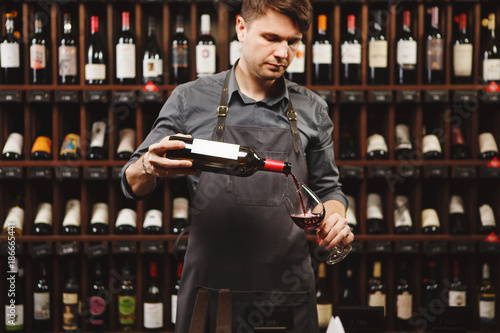 Fotografija Male sommelier pouring red wine into long-stemmed wineglasses.