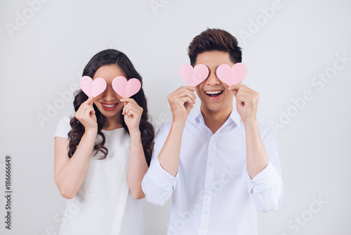 Happy young Vietnamese couple is holding pink paper hearts and smiling