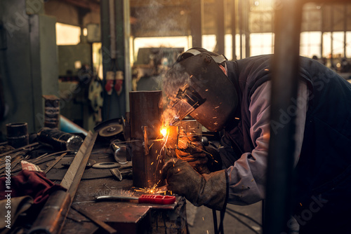 Close up focus side view of professional mask protected welder working in the workshop.