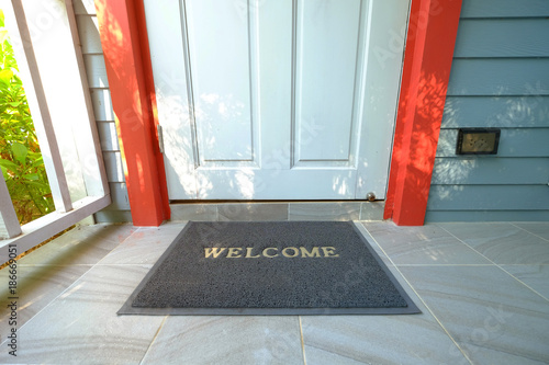 Welcome doormat in front of the wooden door nearby a green garden photo