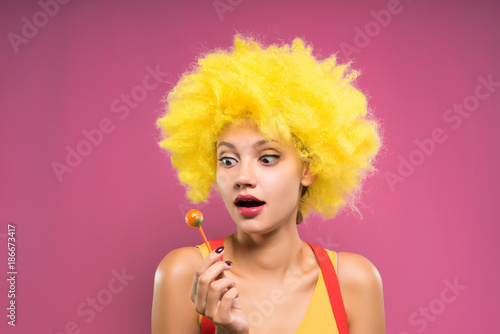 Funny young girl in a wig eats chupa chups photo