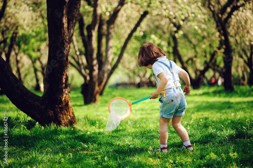 happy 3 years old child boy catching butterflies with net on the walk in sunny garden or park. Spring and summer outdoor activities, happy childhood concept.