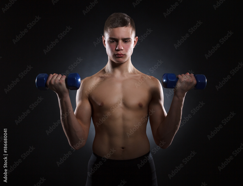 Muscular young man with dumbbells on a dark background. Muscular young man with dumbbells on a dark background.