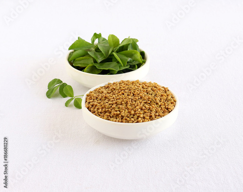 Methi or fenugreek seeds in a bowl and in the background is bowl of methi leaves.