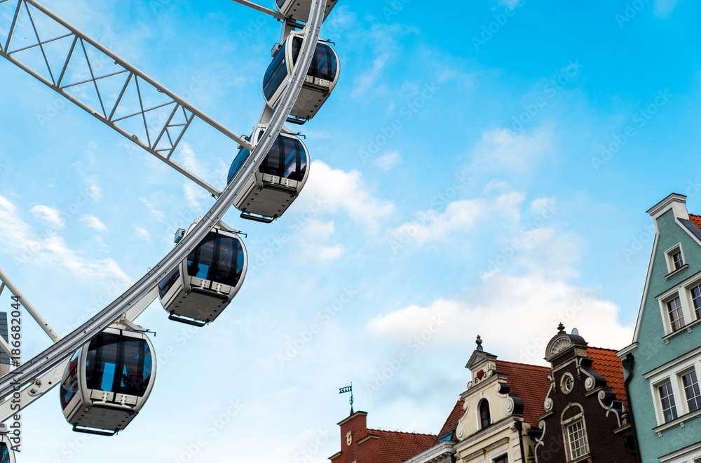 Obraz premium Gdansk, Poland - August 10, 2017: Big ferris wheel in the old town of Gdansk, blu sky background. Center or old town in Gdansk, European polish culture city near baltic sea. Summer travel in Poland.