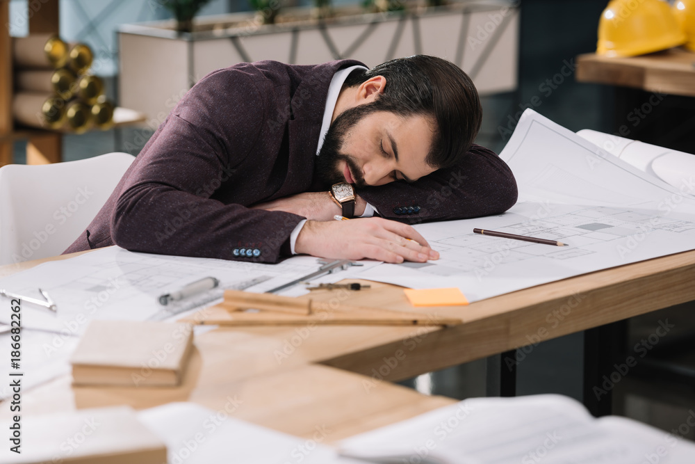 overworked young architect sleeping on building plans at workplace overworked young architect sleeping on building plans at workplace