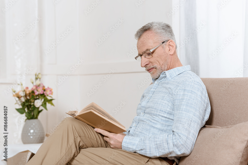 Senior man reading book on sofa in cozy room Senior man reading book on sofa in cozy room