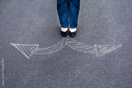 Woman in shoes standing on the asphalt road. On the road with chalk drawn signs arrows. 