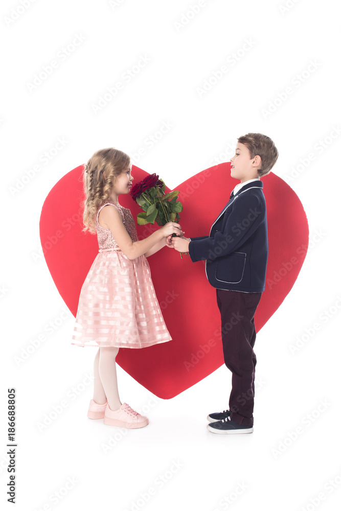 side view of cute little boy presenting flowers to adorable little girl and big red heart symbol behind isolated on white side view of cute little boy presenting flowers to adorable little girl and big red heart symbol behind isolated on white