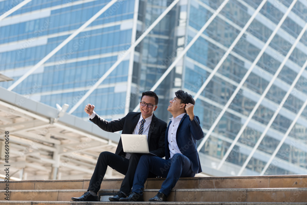 Asian two businessman happy while siting see laptop. in the business district background Asian two businessman happy while siting see laptop. in the business district background