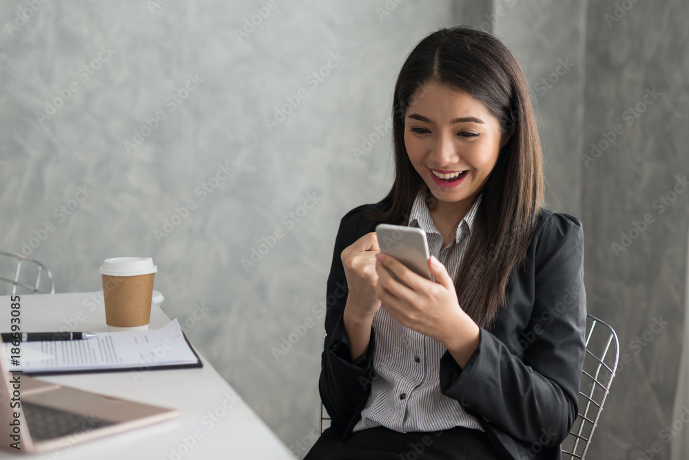 Excited asian business girl while reading a smart phone sitting in her workstation. Business Success Concept Excited asian business girl while reading a smart phone sitting in her workstation. Business Success Concept