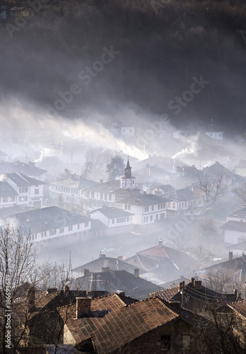 Mountain town in clouds of fog and smoking chimneys early morning