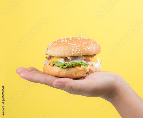 Hand holding tasty hamburger against yellow background,Close up