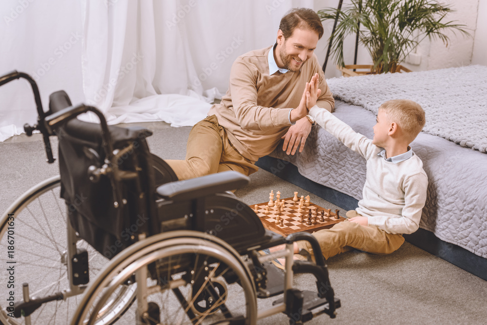 father with disability and son playing chess and giving high five father with disability and son playing chess and giving high five