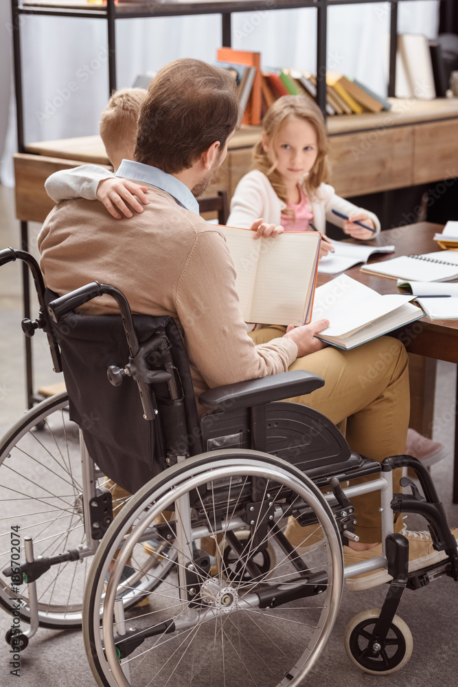 father on wheelchair teaching kids at home and hugging son father on wheelchair teaching kids at home and hugging son