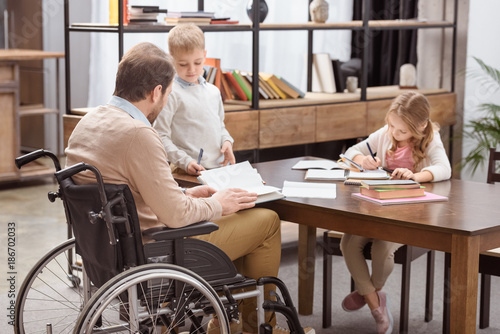 father on wheelchair helping kids with education at home © LIGHTFIELD STUDIOS
