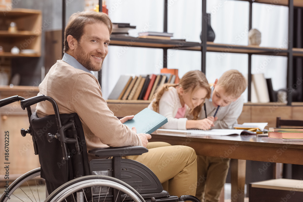smiling father on wheelchair teaching children at home and looking at camera smiling father on wheelchair teaching children at home and looking at camera