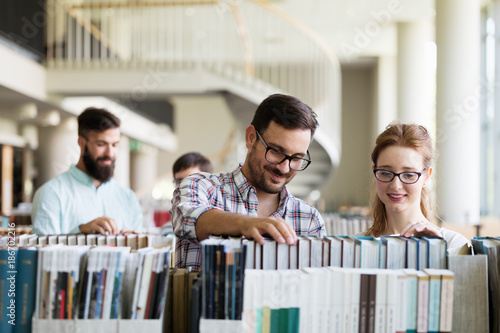 Happy young university students studying with books in library