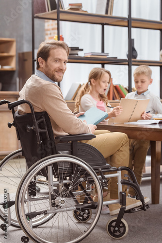 father on wheelchair teaching children at home and looking at camera
