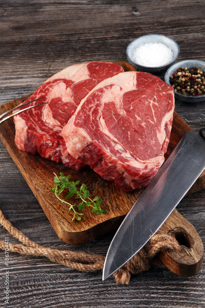 Raw fresh meat Ribeye Steak, seasoning and meat fork on dark bac