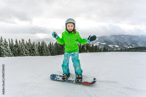 Cute child girl is snowboarding on the snow mountain photo