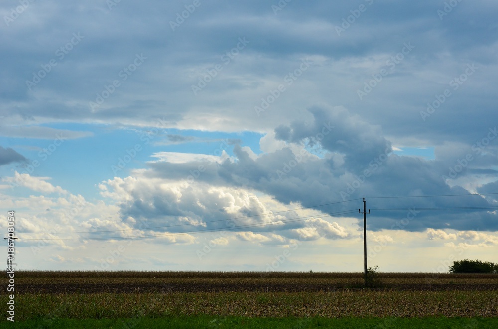 field with dramatic clouds and sky before storm and electric poles in distant field with dramatic clouds and sky before storm and electric poles in distant